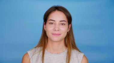 Gri tişörtlü güzel mutlu kadın kameraya bakar ve mavi arka planda gülümser.