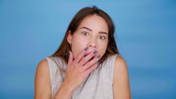 Femme choquée se tourne vers la caméra couvrant la bouche avec la paume sur fond bleu — Video