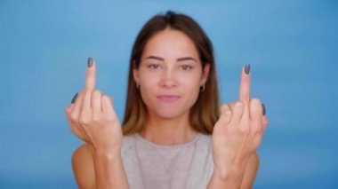 Gri tişörtlü olumlu kadın gülümseme dansları mavi arka planda orta parmak ve fotokopi alanı gösteriyor. 4K yavaş çekim görüntüleri