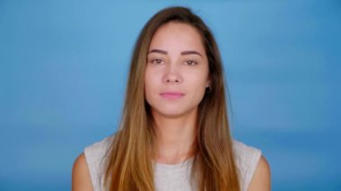 Gri tişörtlü güzel kadın hava öpücüğü yolluyor ve mavi arka planda fotokopi çekerek gülümsüyor. 4K yavaş çekim görüntüleri