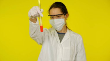 Tıbbi maskeli, gözlüklü ve lateks eldivenli doktor tüpteki testlere bakar.