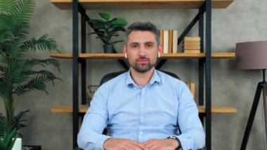 Ofisteki kendine güvenen iş adamı, kablosuz kulaklık takıyor, kamera dinliyor uzaktan görüntülü sohbet konferansı ve web kamerası konseptiyle potansiyel bir çalışanla görüşme yapıyor.