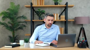 Erkek öğrenci öğretmenini uzaktan dinliyor konferans görüntülü konuşma web kameralı sohbet kahve içiyor, uzaktan eğitim alıyor. Ofisteki adam kablosuz kulaklık takıyor dizüstü bilgisayar başlıkları kullanıyor.
