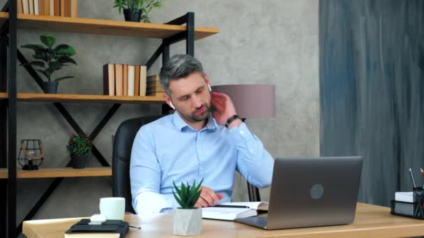 疲惫的商人坐在家里办公室的椅子上 长时间使用笔记本电脑后 他身穿无线耳机 头颈酸痛 肌肉紧张 体态不佳 需要治疗 — 图库视频影像