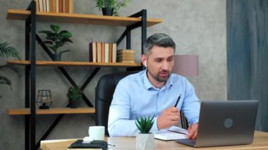 Gülümseyen uzaktan kumandalı erkek öğretmen kablosuz kulaklıkla öğrencilerle iletişim kuruyor video konferans web kamerası dizüstü bilgisayarı. Gri saçlı sakallı adam öğrencileri motive eder. Yavaş çekim