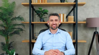 Ofisteki masada oturan, kablosuz kulaklık takan, mutlu gülümseyen iş adamı kameraya bakar görüntülü konuşma konferansında interinterlocutor dinler, web kamerası konsepti.