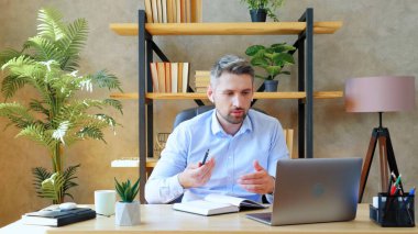 Evde kablosuz kulaklık takan bir adam uzaktan video konferans görüşmesi yapıyor.