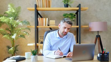 Yurt içi ofis çalışmasındaki adam öğretmeniyle çevrimiçi video görüşmesi yapıyor.