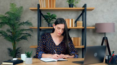 Kadın deftere uzaktan görüntülü konferans üzerine yazıyor. Öğretmenle sohbet ediyor.