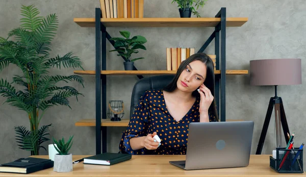 Zakenvrouw zitten op stoel aan tafel in het thuiskantoor zet op draadloze oortelefoon — Stockfoto