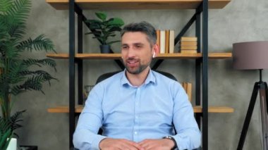 Ofisteki gülümseyen gri saçlı iş adamı kablosuz kulaklık takıyor koltukta oturup yan tarafa bakıyor ve tamam diyor. 4K yavaş çekim görüntüleri