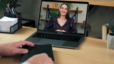 Bilgisayar ekranı konuşmalarında kadın öğretmenlik uzak bir web kamerası ve uzaktan eğitim ile öğretiyor. Erkek öğrenci konferans odasında internetten ders çalışıyor. Bilgisayarı arıyor. Not defterine yazıyor.