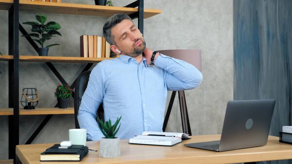 Tired man massages neck after using laptop computer long time, poor posture