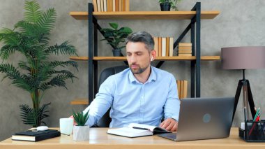 Ev ofisteki masada oturan adam uzaktan kumandalı bilgisayar kullanıyor.