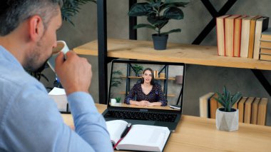 Erkek, konferans odasında internetten bilgisayar başında ders çalışıyor, kahve içiyor.