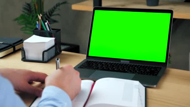 Man Student Studie schreibt Informationen in Notizbuch. Laptop mit grünem Bildschirm — Stockvideo