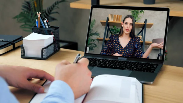 Erkek öğrenci çevrimiçi video arama bilgisayarı ile çalışır, deftere yazar