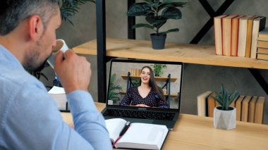 Erkek öğrenci çevrimiçi konferans videosu bilgisayarında çalışıyor, kahve içiyor.