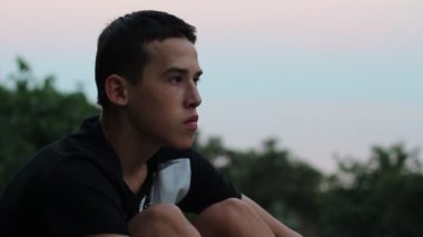 Genç çocuk yalnız üzgün veya endişeli bakarak oturur. Üzgün üzgün genç günbatımında oturan adam. Akşam şehir