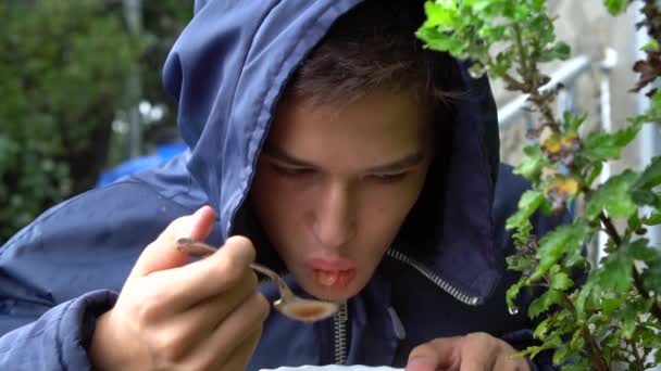 一个十几岁的孩子正在外面的雨中吃饭 — 图库视频影像