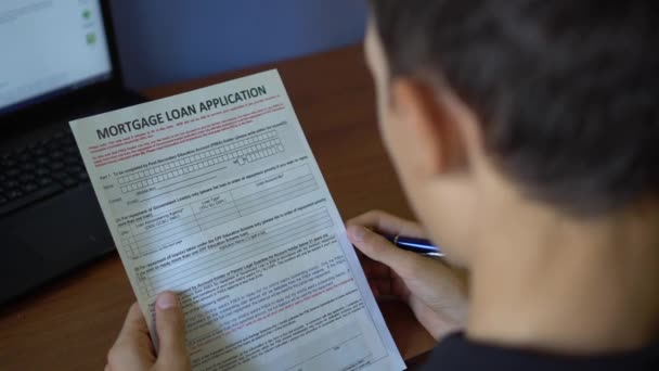 一个年轻人正在申请抵押贷款 在纸页上的信用申请表 — 图库视频影像