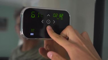 Programlanabilir bir oda termostatı ayarlım. Bir adam dokunmatik paneldeki sıcaklığı ayarlar.