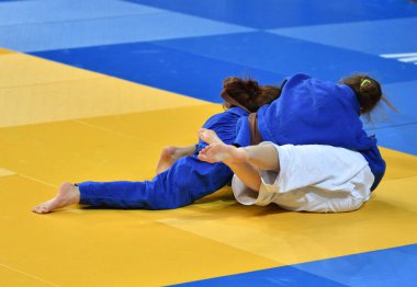 Kimonolu iki kız judoka tatamide yarışıyor.