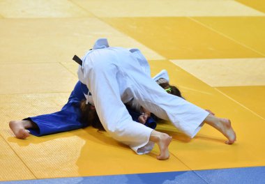 Kimonolu iki kız judoka tatamide yarışıyor.