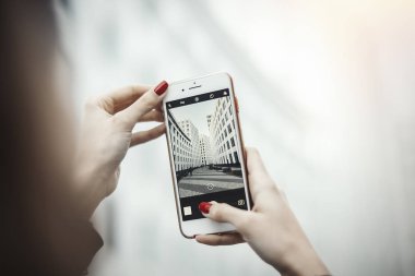 Young attractive girl making photo of skyscraper by mobile phone. clipart