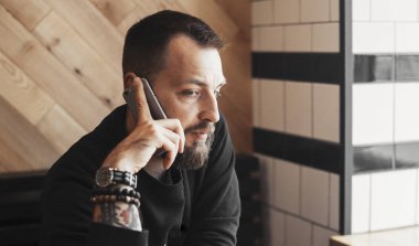 Kafede telefonla konuşan genç dövmeli adam yakın çekim.