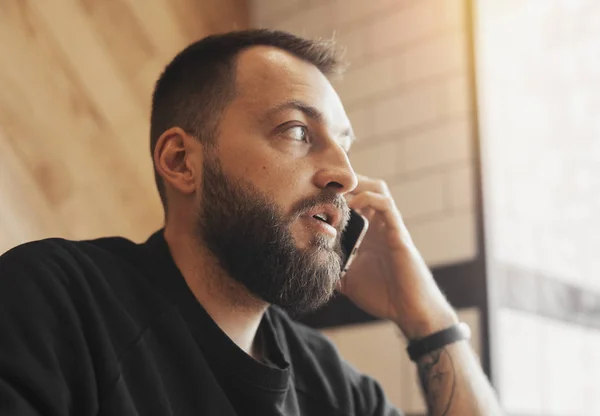 Barbudo atractivo hombre hablando por teléfono en la cafetería . — Foto de Stock