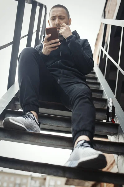 Nuori mies istuu tikkailla ja katselee matkapuhelintaan. . — kuvapankkivalokuva