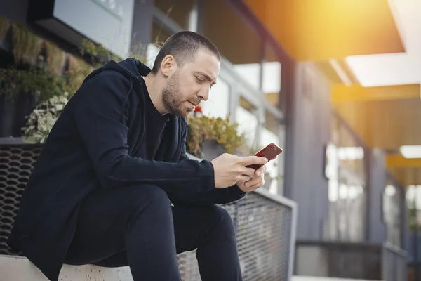 Barbudo hombre sentado en un paso y mirando a la pantalla del teléfono móvil . — Foto de Stock
