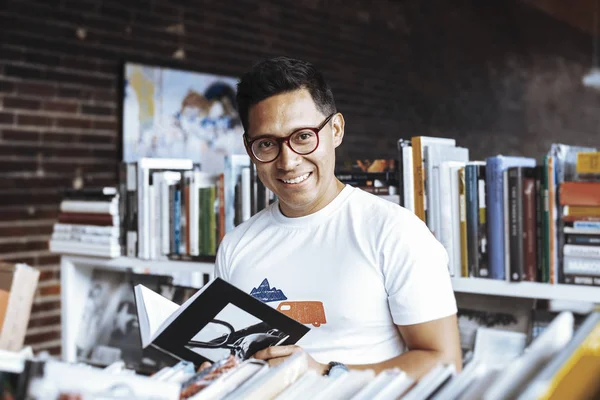 Young spectacled man reading book in a book store. — Stock Photo, Image