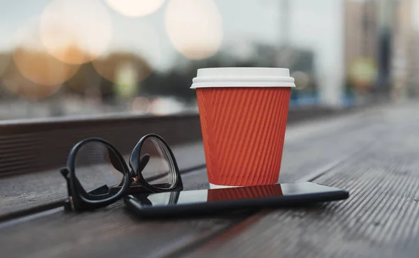 Close up of red coffee cup, mobile phone and glasses.