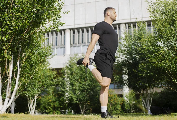 Homme attrayant faisant des exercices d'étirement des jambes avec les mains dans le parc . — Photo