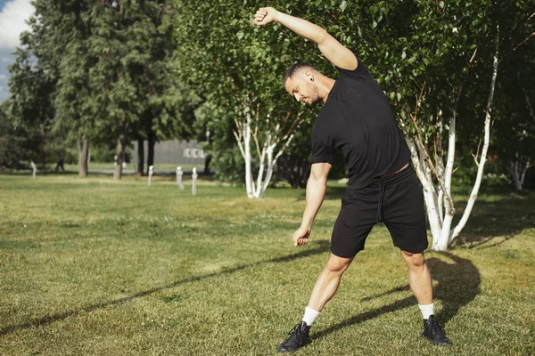 Hombre atractivo haciendo ejercicios de estiramiento con las manos en el parque . — Foto de Stock