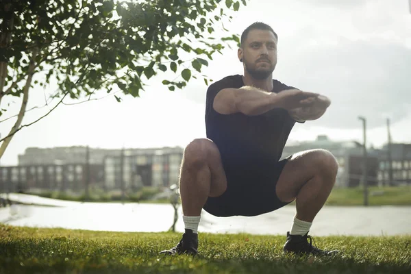 Jeune homme attrayant accroupi en plein air dans le parc avec les mains tendues . — Photo