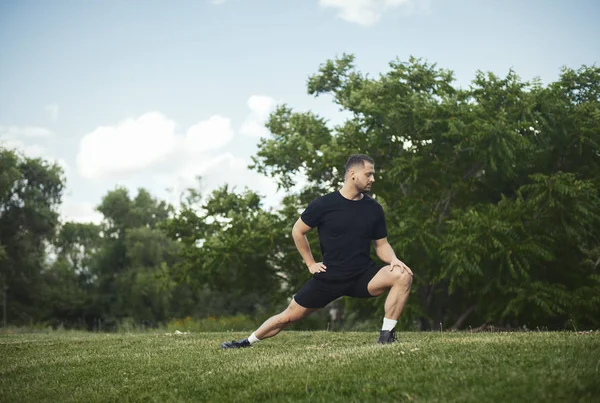 Jeune homme séduisant faisant fente en plein air dans le parc. Vue latérale, plan lointain . — Photo