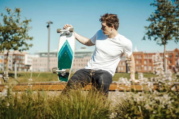 Vonzó fiatalember ült a padon, és a gazdaság longboard. — Stock Fotó