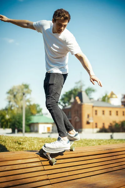 Joven hombre atractivo en camiseta blanca montando longboard en el parque . —  Fotos de Stock