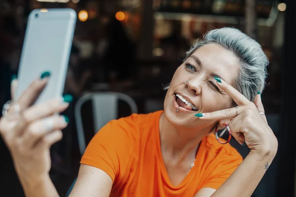Attraktiva blonda kvinnan att göra selfie på café och visar tecken på seger — Stockfoto
