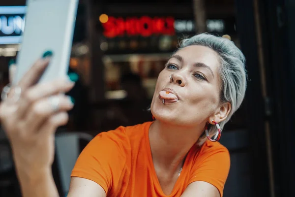 Attraktiva blonda flicka i orange T-shirt gör selfie på café — Stockfoto
