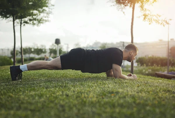 Plan lejano de joven atractivo ejercitando tablón al aire libre . — Foto de Stock