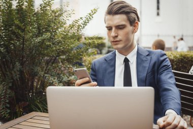 Mobil telefon elinde tutarak ve laptop yanında oturan iş adamı. Önden görünüm