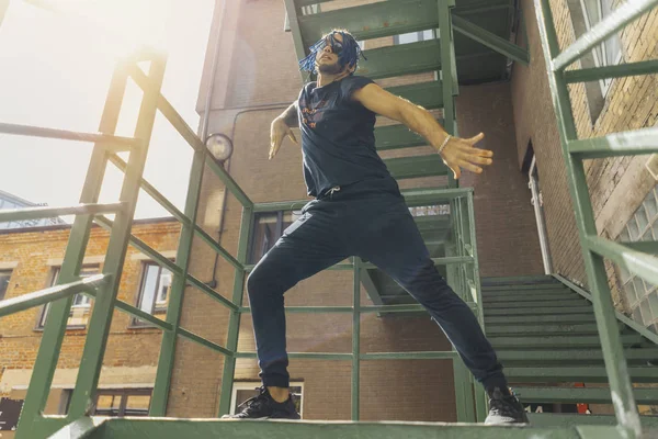Młody człowiek z niebieski dredy tańca reggaeton na schodach zielony. — Zdjęcie stockowe