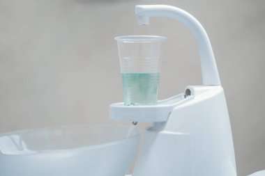 Beyaz diş hekimi tükürük hokkası ve ışık yeşil su ile plastik kap kapatmak.