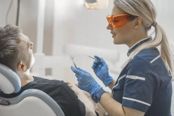 Close up de mulher dentista sorrindo para um cliente e segurando instrumentos dentários . — Fotografia de Stock