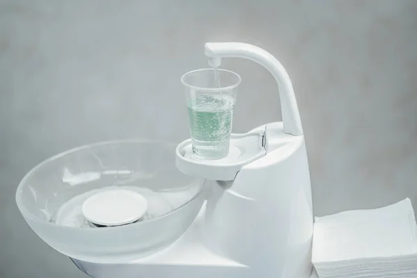 Zblízka bílý zubař plivátka a kelímek s světle zelená voda. — Stock fotografie