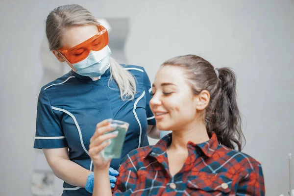 A nő a fogorvos adó műanyag pohár vizet, hogy egy ügyfél közelről . — Stock Fotó